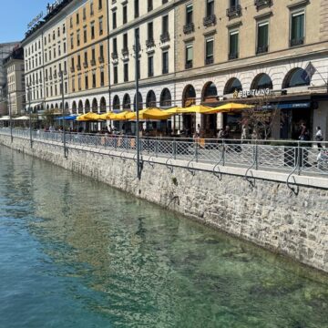 Façades et terrasses aux parasols jaunes sur un quai à Genève.