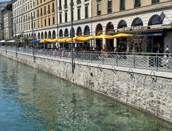 Façades et terrasses aux parasols jaunes sur un quai à Genève.